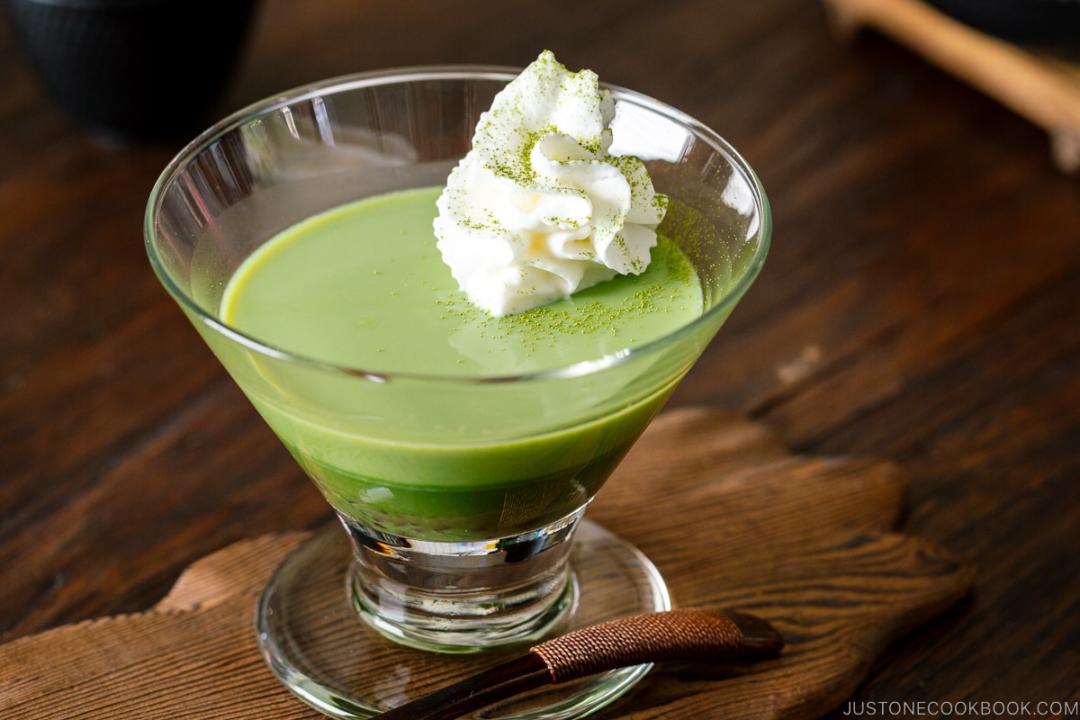 A glass containing matcha pudding with whipped cream.