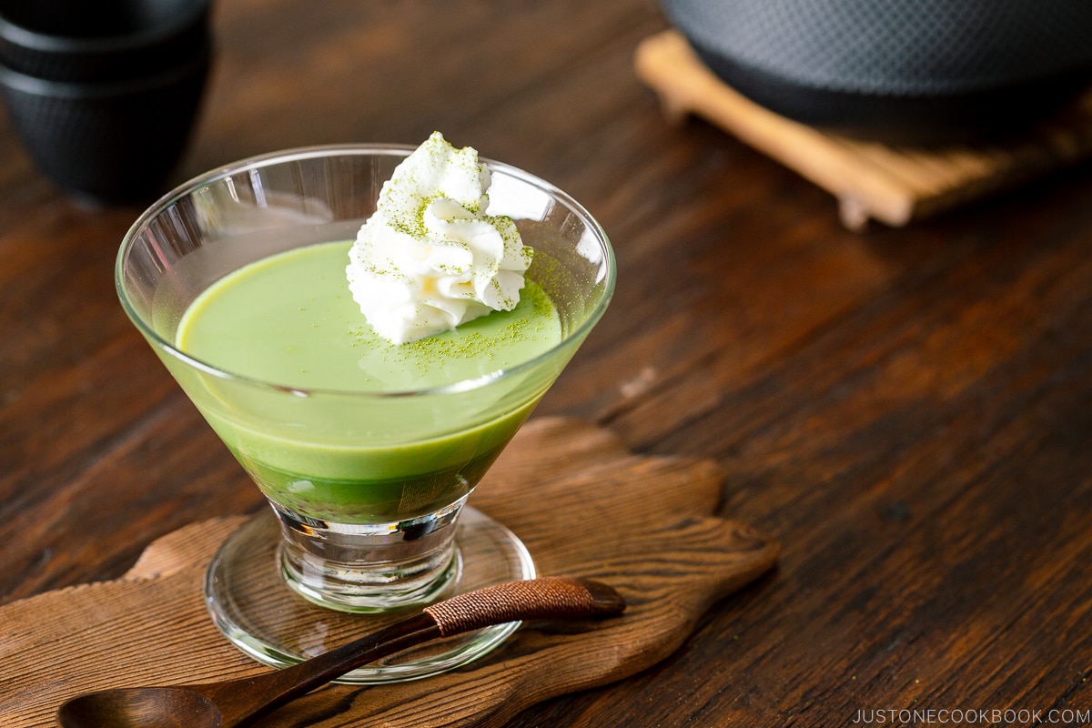 A glass containing matcha pudding with whipped cream.