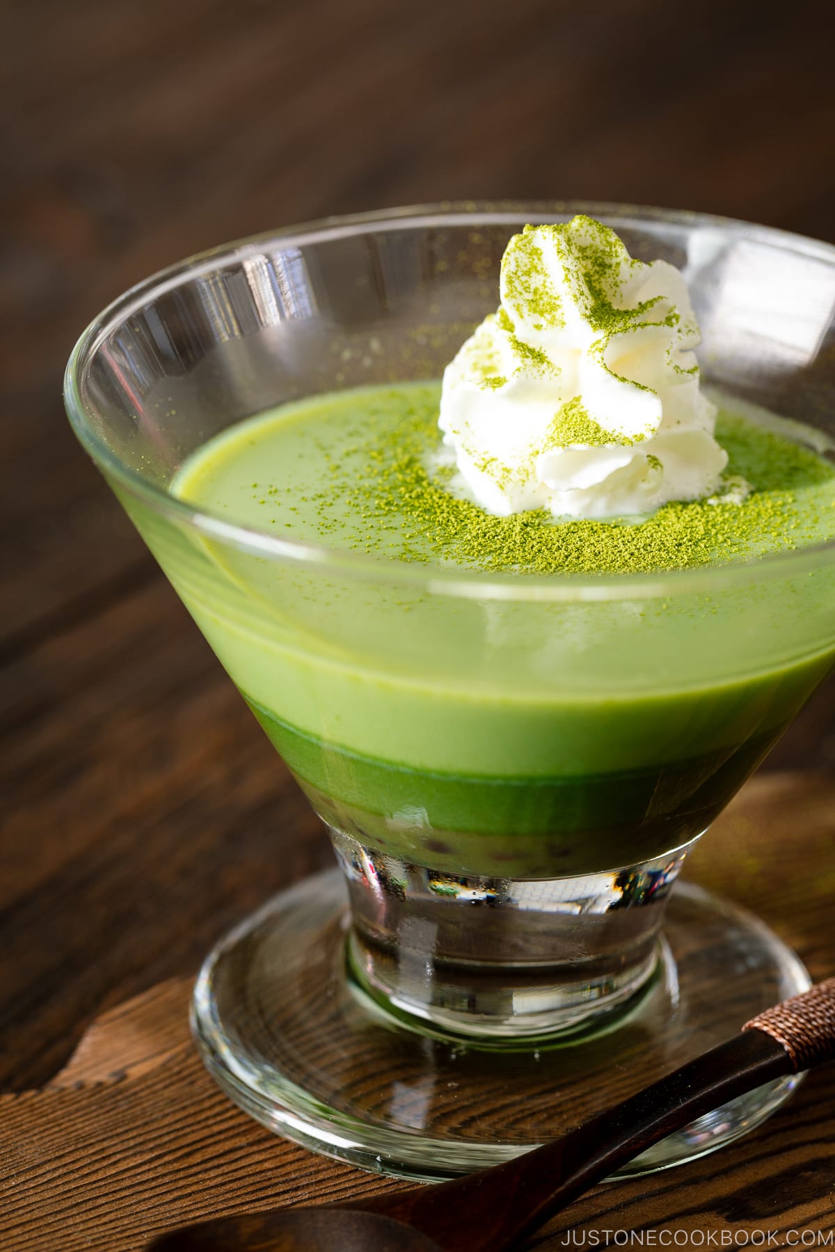 A glass containing matcha pudding with whipped cream.