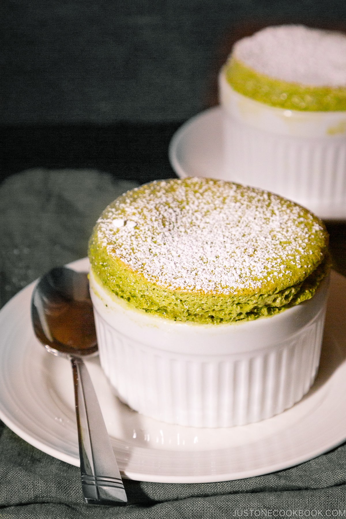 A white ramekin containing matcha souffle dusted with powdered sugar.