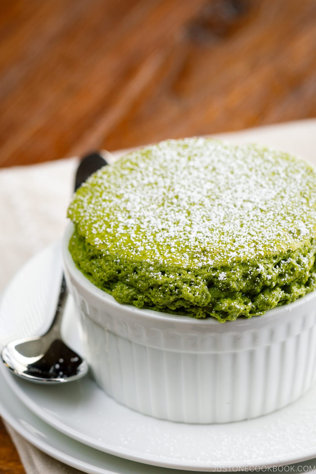 A white ramekin containing matcha souffle dusted with powdered sugar.