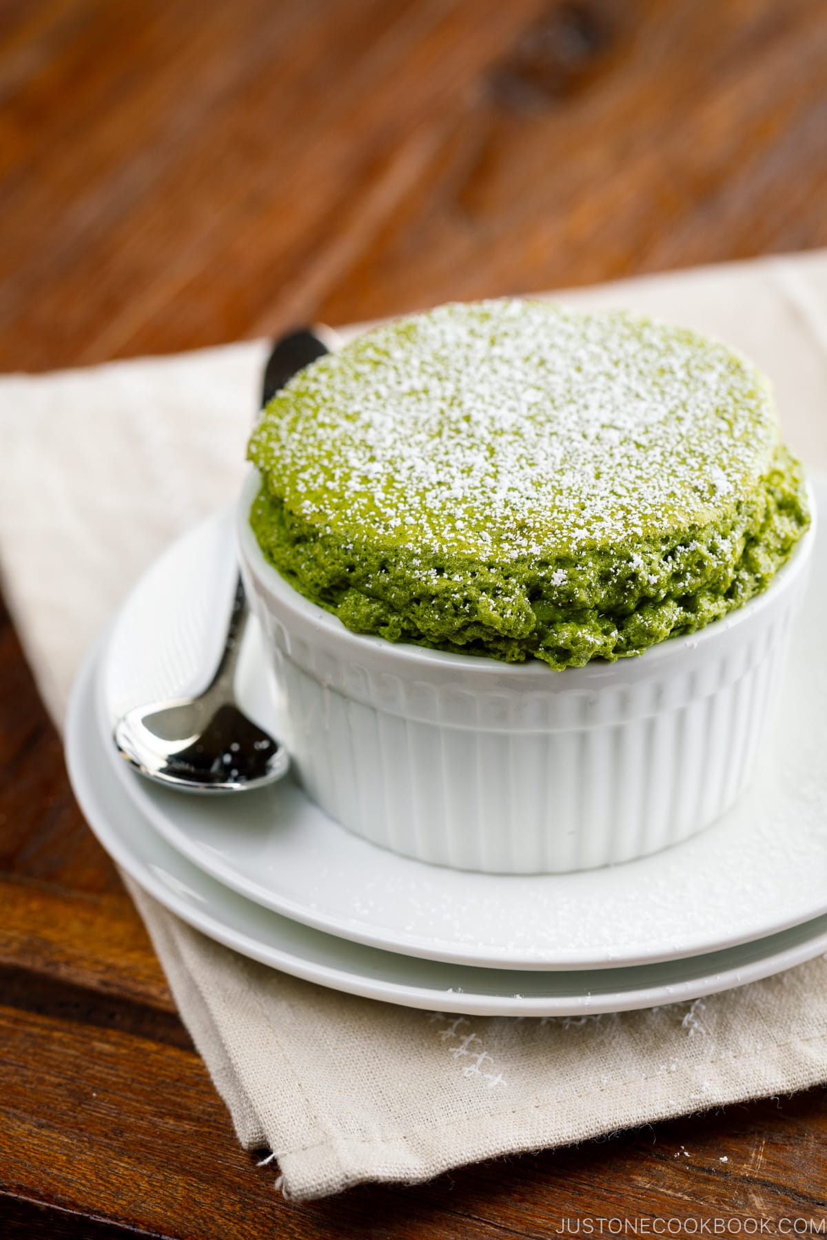 A white ramekin containing matcha souffle dusted with powdered sugar.