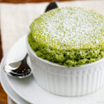 A white ramekin containing matcha souffle dusted with powdered sugar.