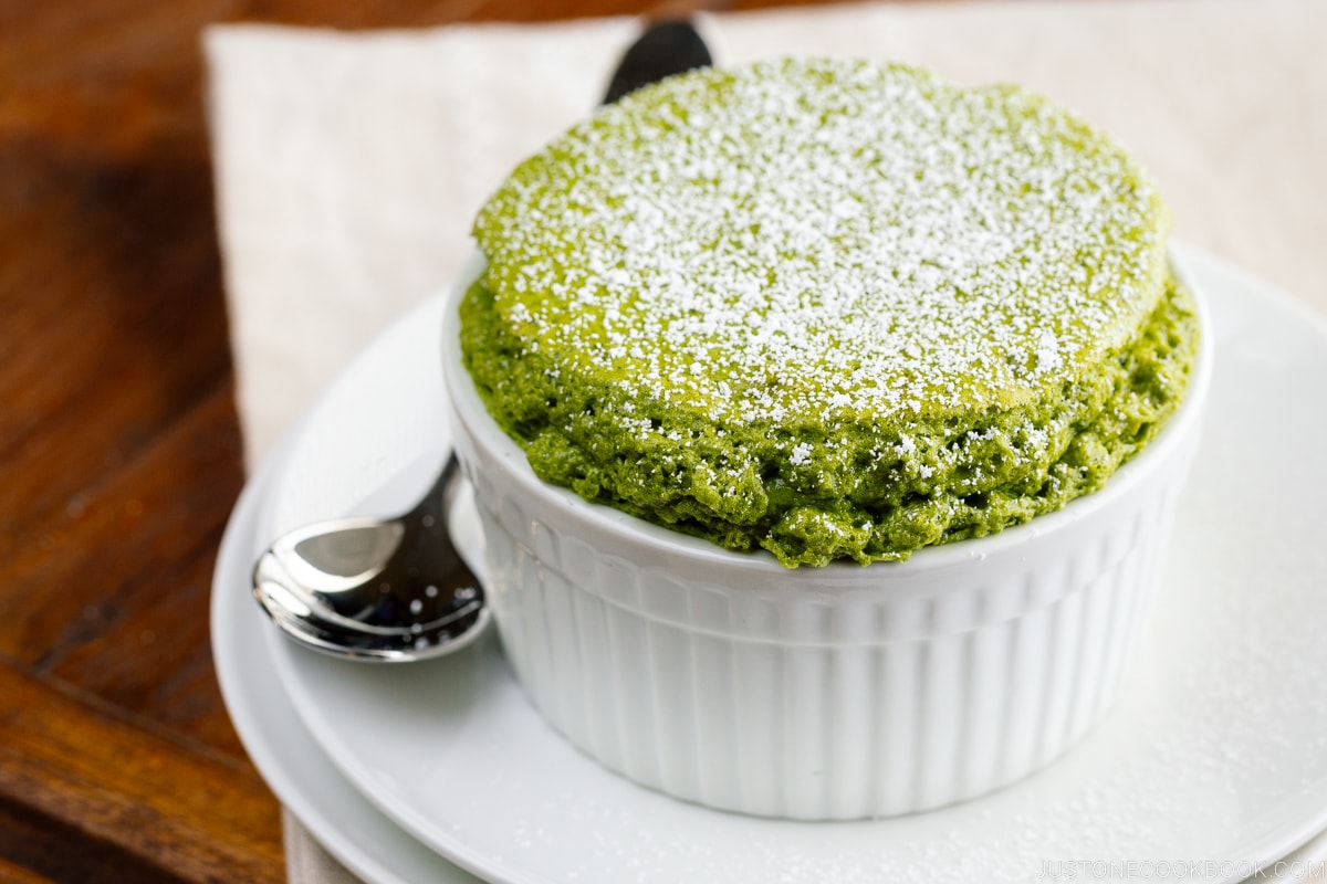 A white ramekin containing matcha souffle dusted with powdered sugar.