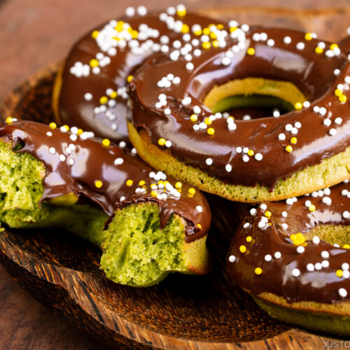 A wooden plate containing matcha donuts.