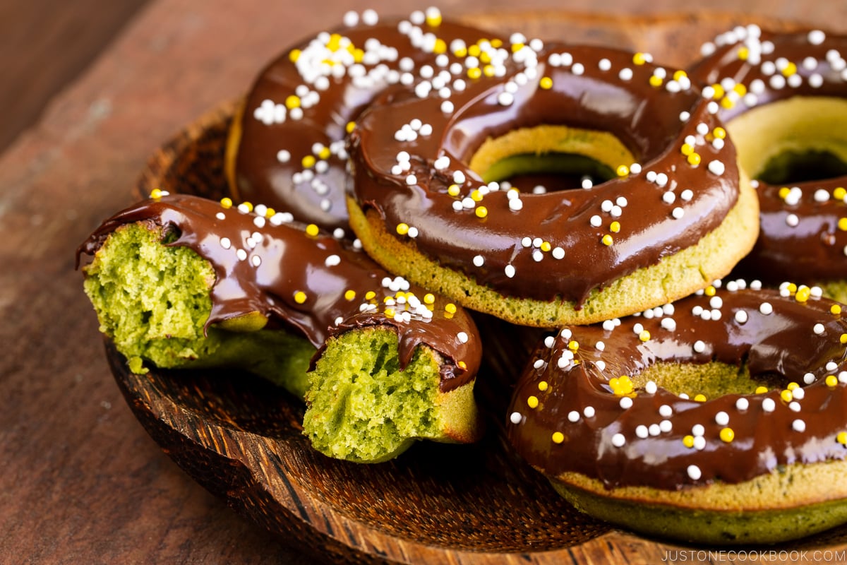 A wooden plate containing matcha donuts.