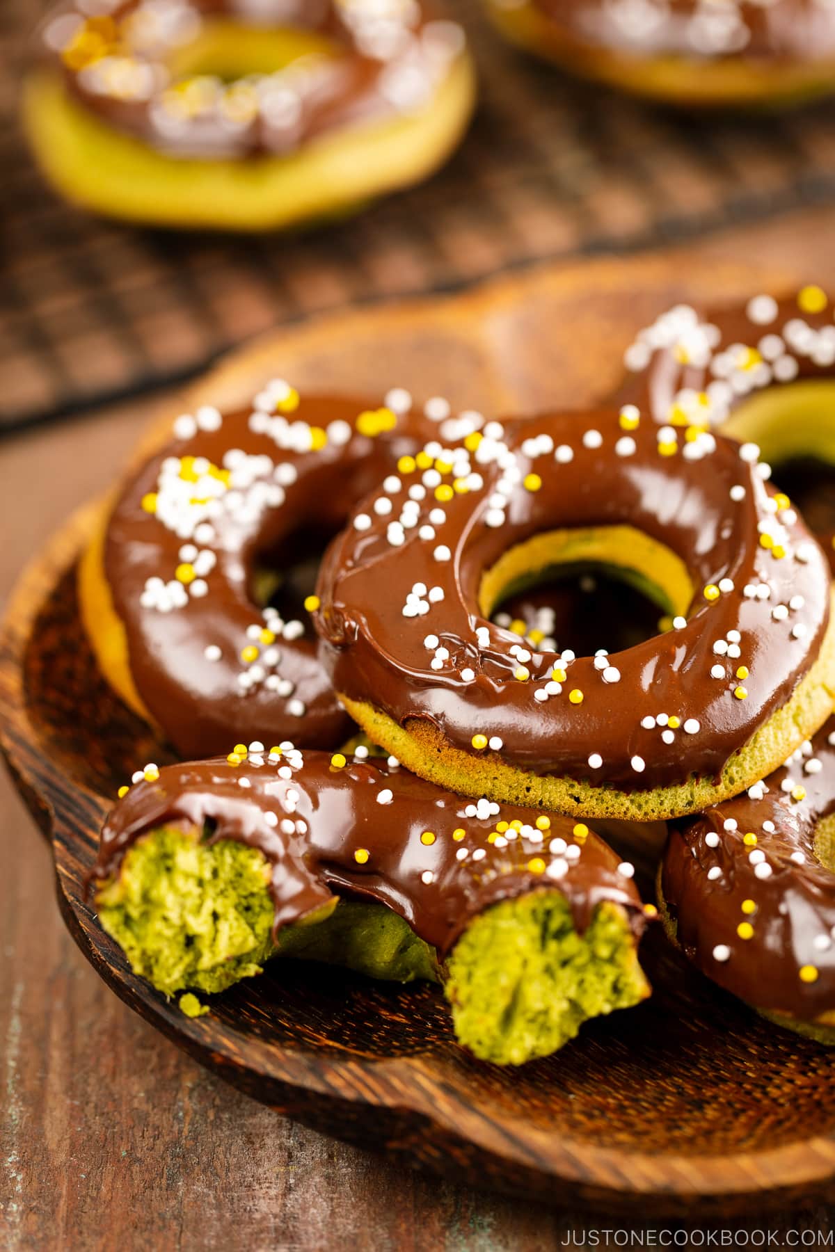 A wooden plate containing matcha donuts.