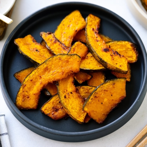 A black round ceramic plate containing roasted kabocha slices.