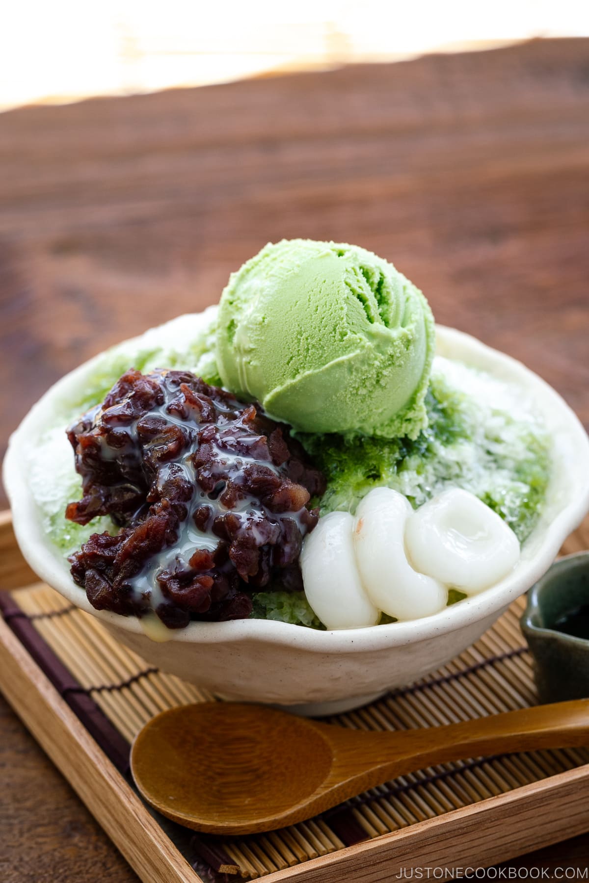 Un bol contenant de la glace pilée, arrosée de sirop de matcha et garnie de pâte de haricots rouges, de shiratama dango, de lait concentré sucré et de crème glacée au thé vert.