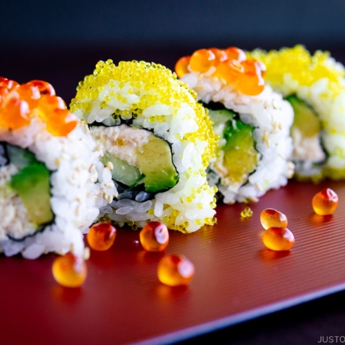 A red platter containing California roll with ikura on top.