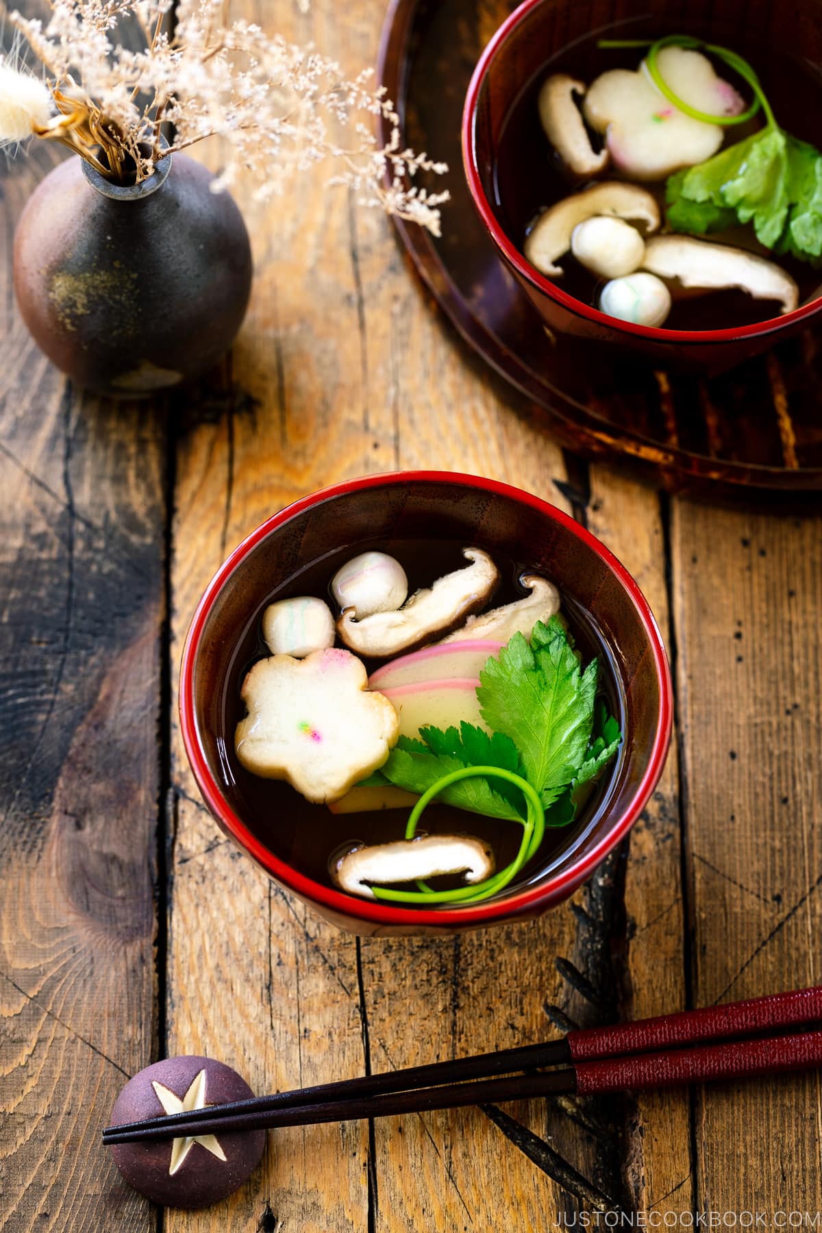 Red Japanese lacquered bowls containing clear soup (Osumashi) with shiitake mushrooms, fu, and mitsuba leaf.