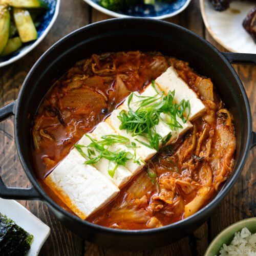 A black staub containing Kimchi Jjigae (Stew) topped with slices of tofu.