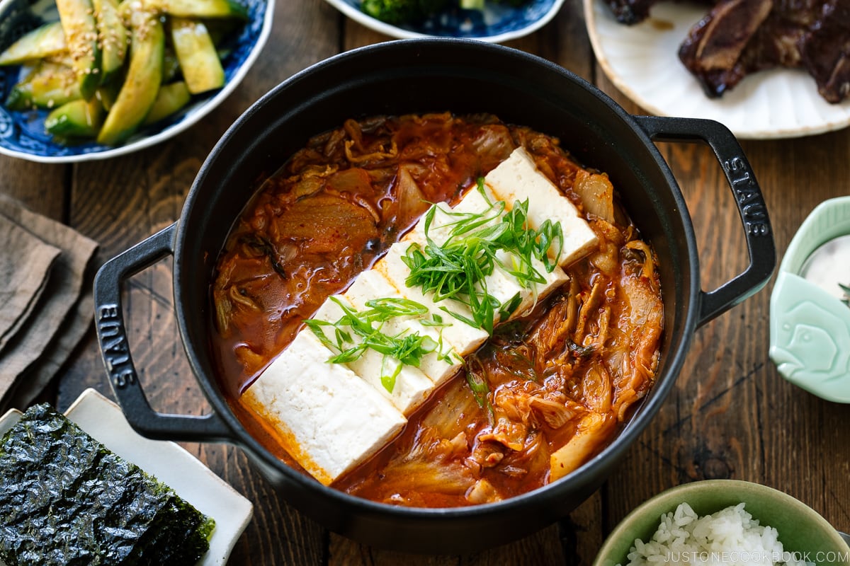 A black staub containing Kimchi Jjigae (Stew) topped with slices of tofu.