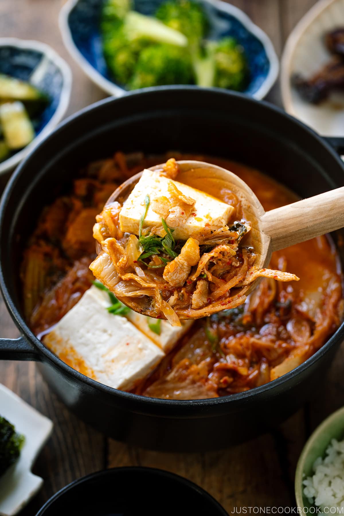 A wooden ladle picking up Kimchi Jjigae from the black Satub pot.