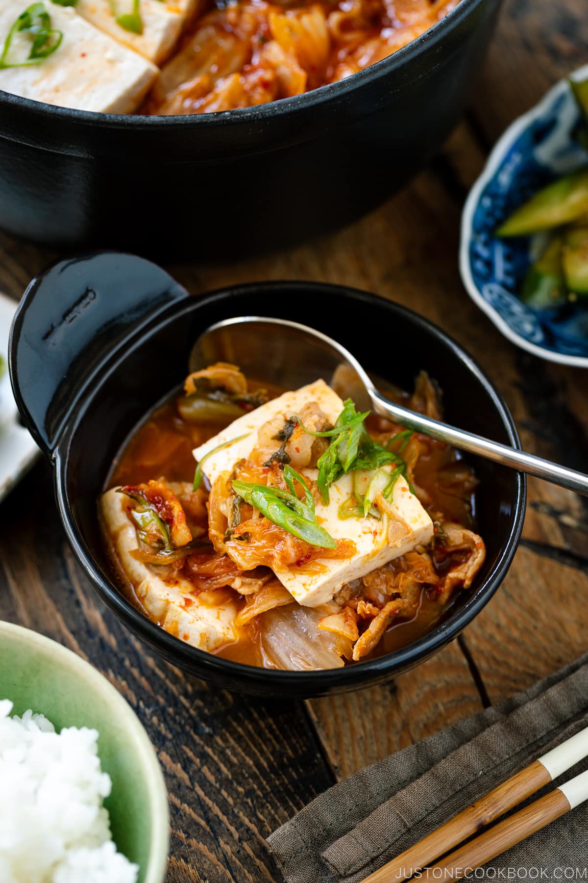 A black bowl containing kimchi jjigae served with a spoon.