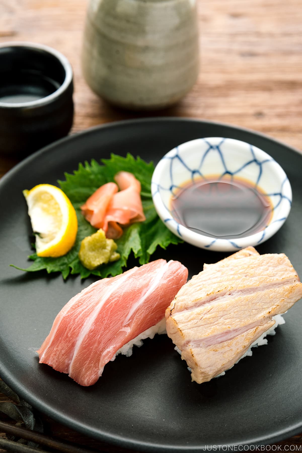 A black plate containing otoro sushi two ways, served with soy sauce, wasabi, and sushi ginger.