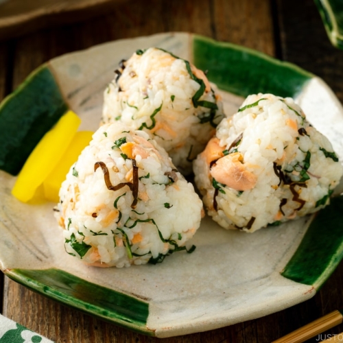 A Japanese ceramic plate containing Salmon and Shio Kombu Onigiri served with daikon pickles.