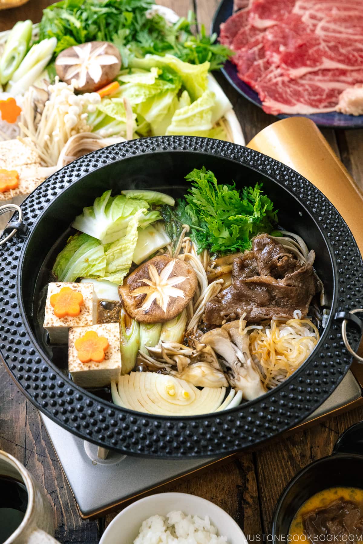 Japanese round cast iron pan containing Sukiyaki, a Japanese hot pot dish where marbled beef, tofu, and vegetables are simmered in sweetened soy sauce broth.