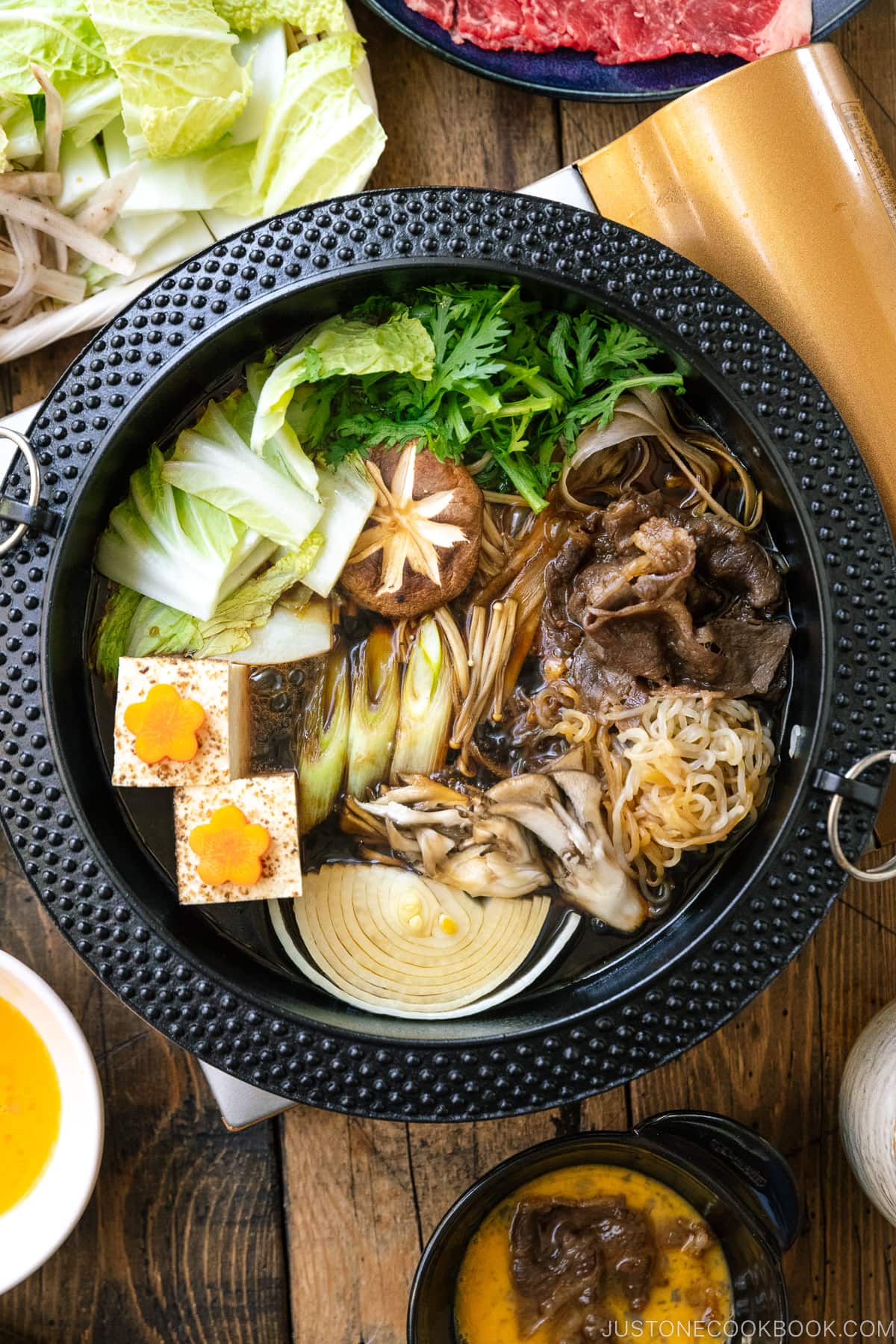 Japanese round cast iron pan containing Sukiyaki, a Japanese hot pot dish where marbled beef, tofu, and vegetables are simmered in sweetened soy sauce broth.