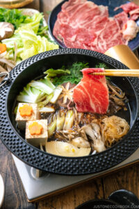 Japanese round cast iron pan containing Sukiyaki, a Japanese hot pot dish where marbled beef, tofu, and vegetables are simmered in sweetened soy sauce broth.