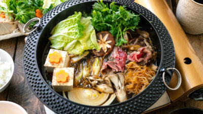 Japanese round cast iron pan containing Sukiyaki, a Japanese hot pot dish where marbled beef, tofu, and vegetables are simmered in sweetened soy sauce broth.