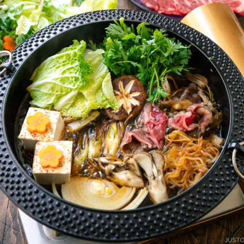 Japanese round cast iron pan containing Sukiyaki, a Japanese hot pot dish where marbled beef, tofu, and vegetables are simmered in sweetened soy sauce broth.