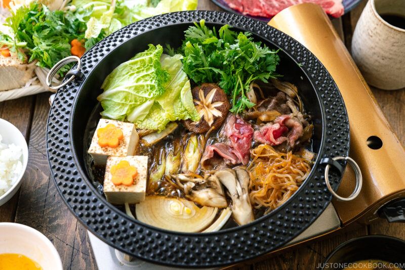 Japanese round cast iron pan containing Sukiyaki, a Japanese hot pot dish where marbled beef, tofu, and vegetables are simmered in sweetened soy sauce broth.