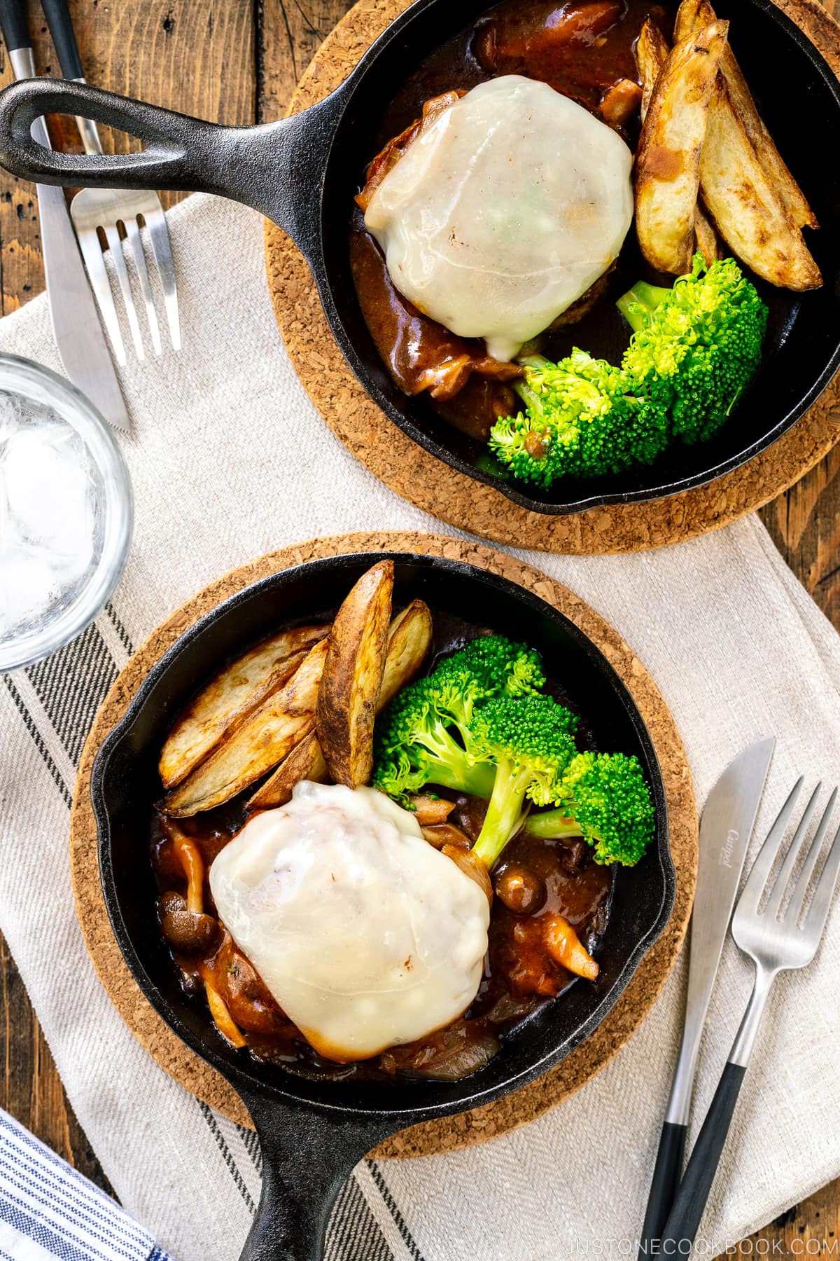 Mini cast iron skillets containing Japanese stewed hamburger steak with melted cheese on top.