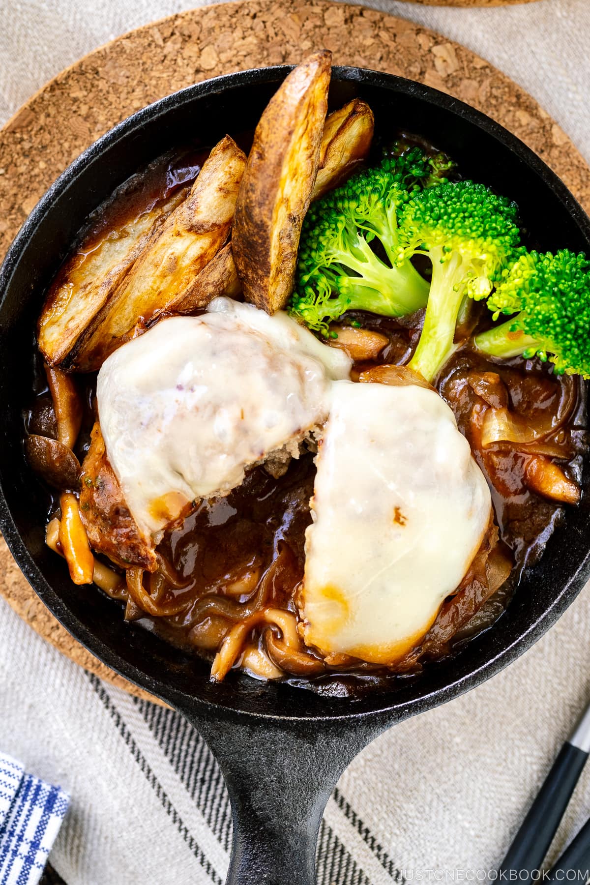 A mini cast iron skillet containing Japanese stewed hamburger steak with melted cheese on top.
