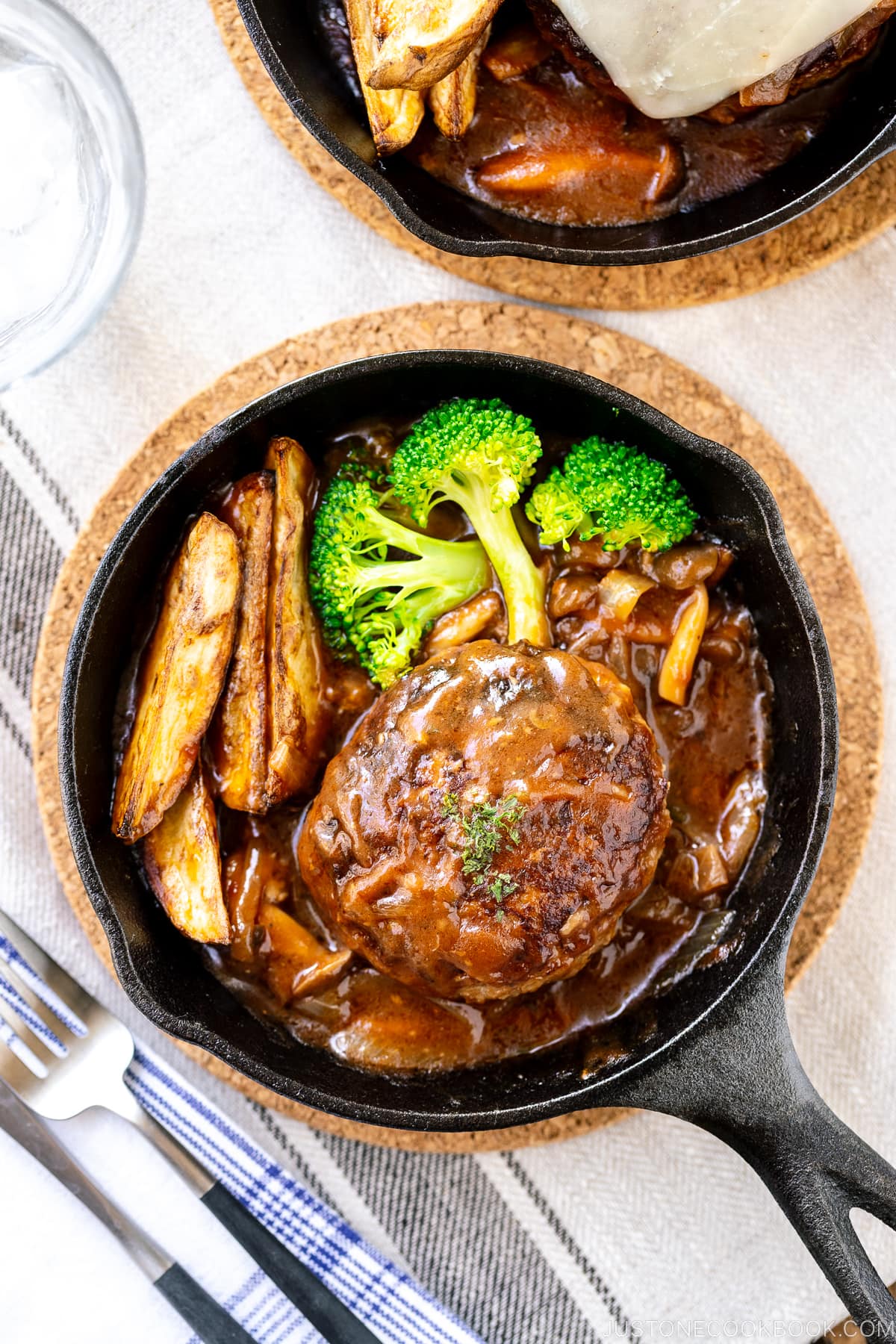 Mini cast iron skillets containing Japanese stewed hamburger steak called Nikomi Hambagu, along with baked potato fries and steamed broccoli.