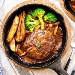 A mini cast iron skillet containing Japanese stewed hamburger steak called Nikomi Hambagu, along with baked potato fries and steamed broccoli.