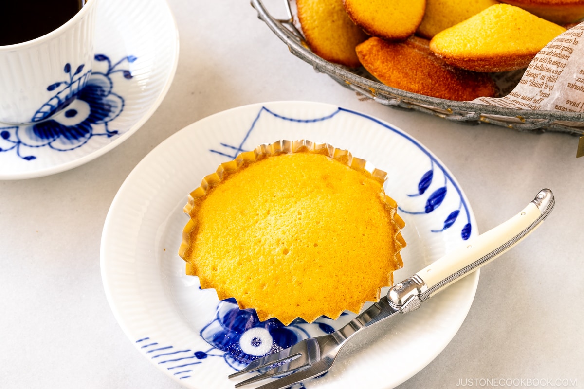 A white plate containing a madeleine in an individual fluted cake pan.