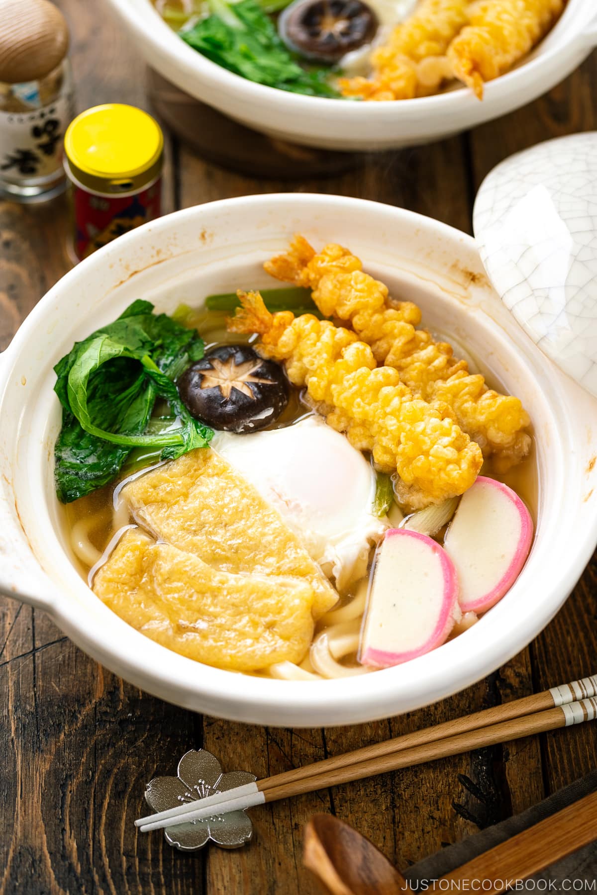 A donabe claypot containing Nabeyaki Udon, which is made of udon noodles, kamaboko fish cake, fried tofu, egg cooked in a dashi broth and topped with shrimp tempura.