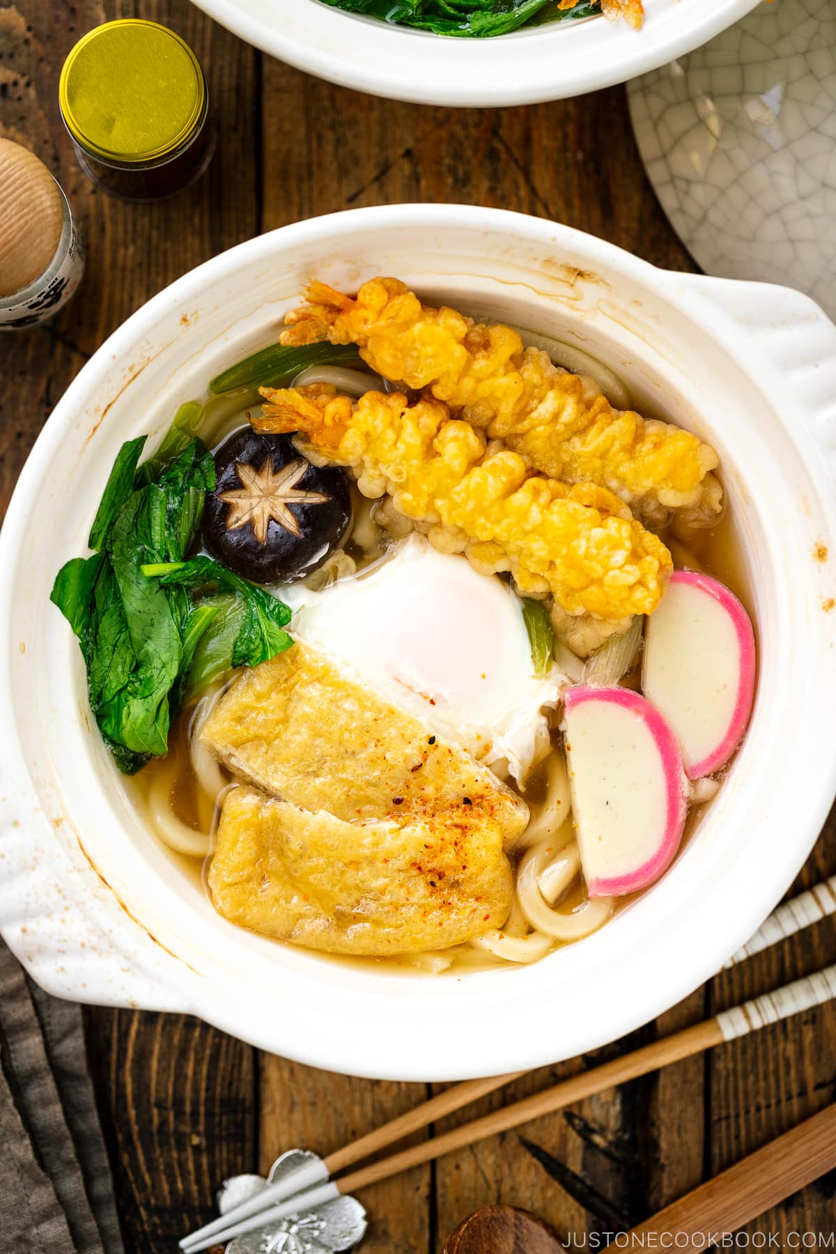 A donabe claypot containing Nabeyaki Udon, which is made of udon noodles, kamaboko fish cake, fried tofu, egg cooked in a dashi broth and topped with shrimp tempura.