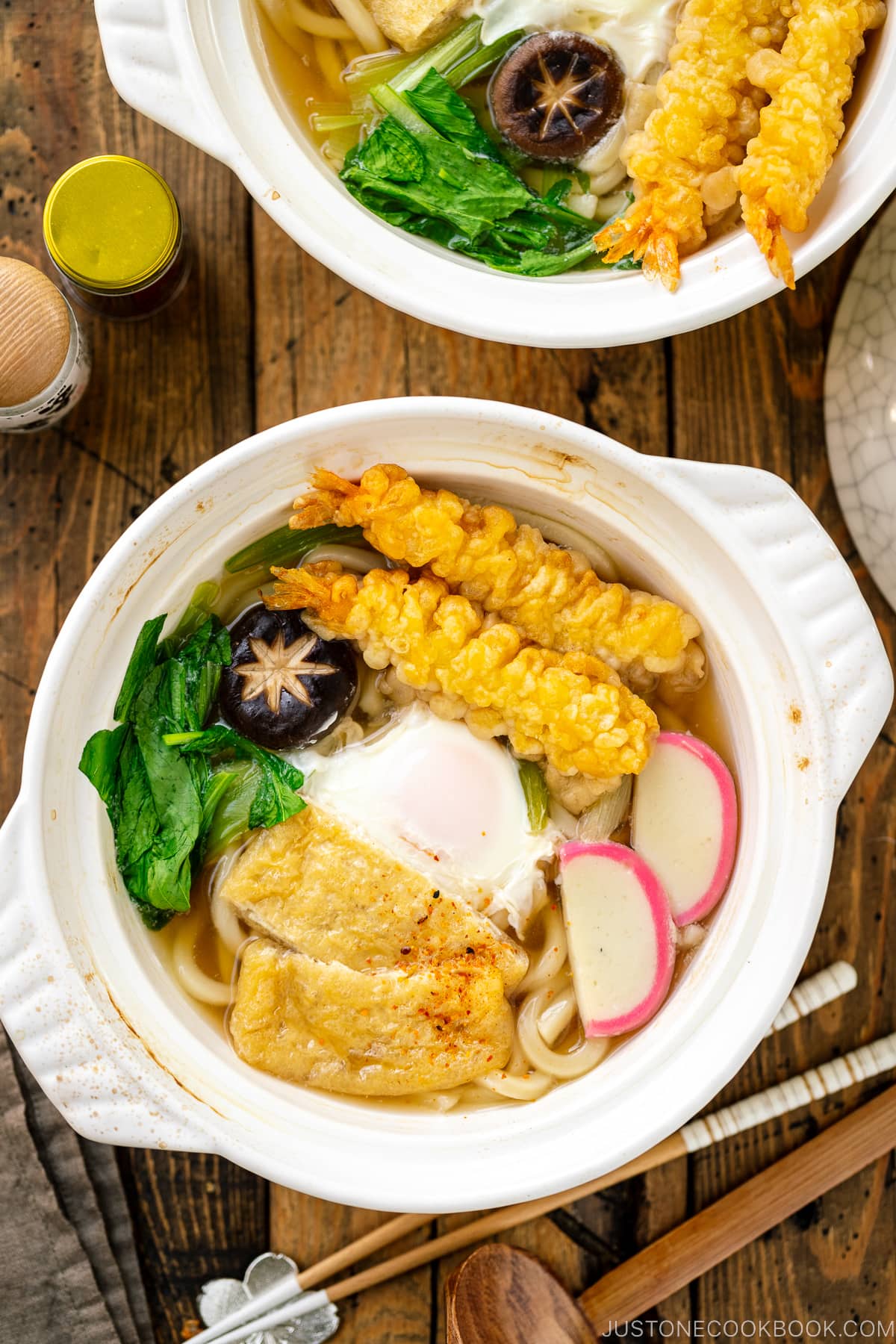 A donabe claypot containing Nabeyaki Udon, which is made of udon noodles, kamaboko fish cake, fried tofu, egg cooked in a dashi broth and topped with shrimp tempura.