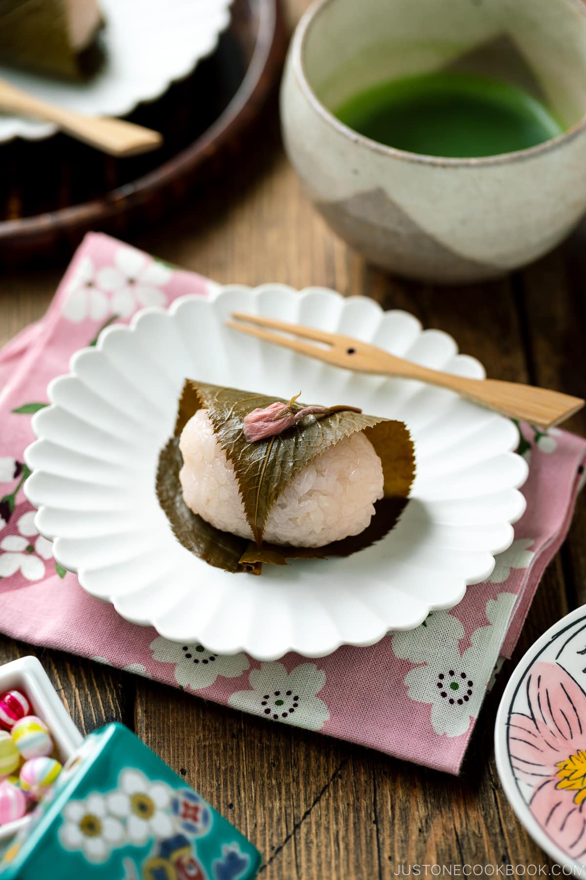 A round fluted plate containing sakura mochi served with matcha tea.