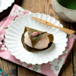 A round fluted plate containing sakura mochi served with matcha tea.