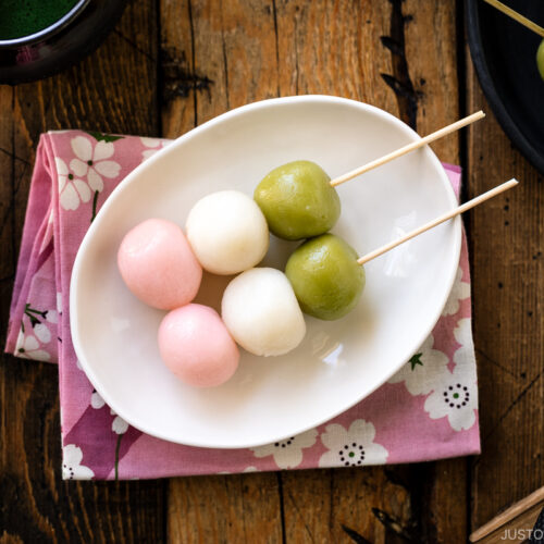 A white oval plate containing two Hanami Dango, served with matcha green tea.