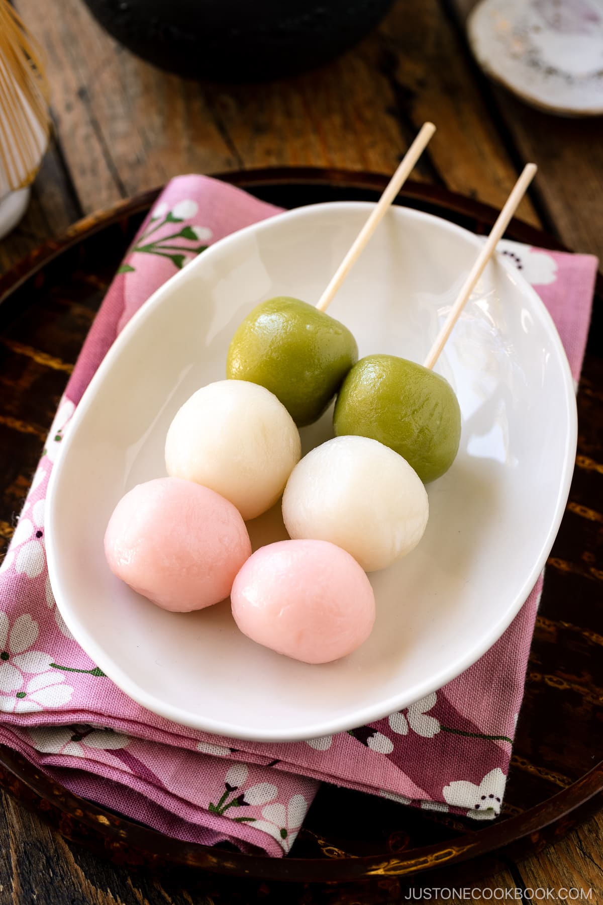 A white oval plate containing two Hanami Dango, served with matcha green tea.