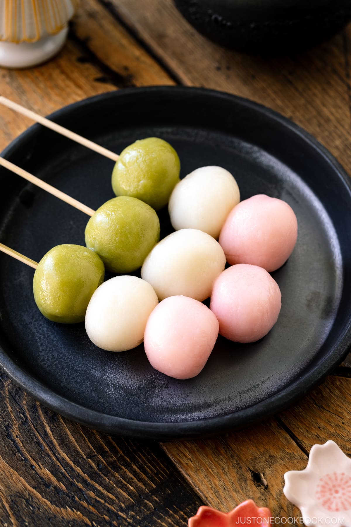 A black rimmed round plate containing two Hanami Dango, served with matcha green tea.