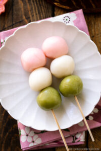 A white fluted round plate containing two Hanami Dango, served with matcha green tea.