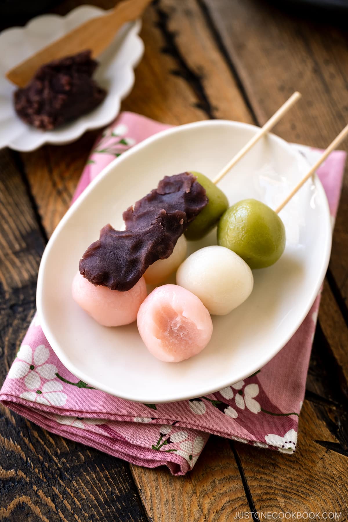 A white oval plate containing two Hanami Dango topped with sweet red bean paste.
