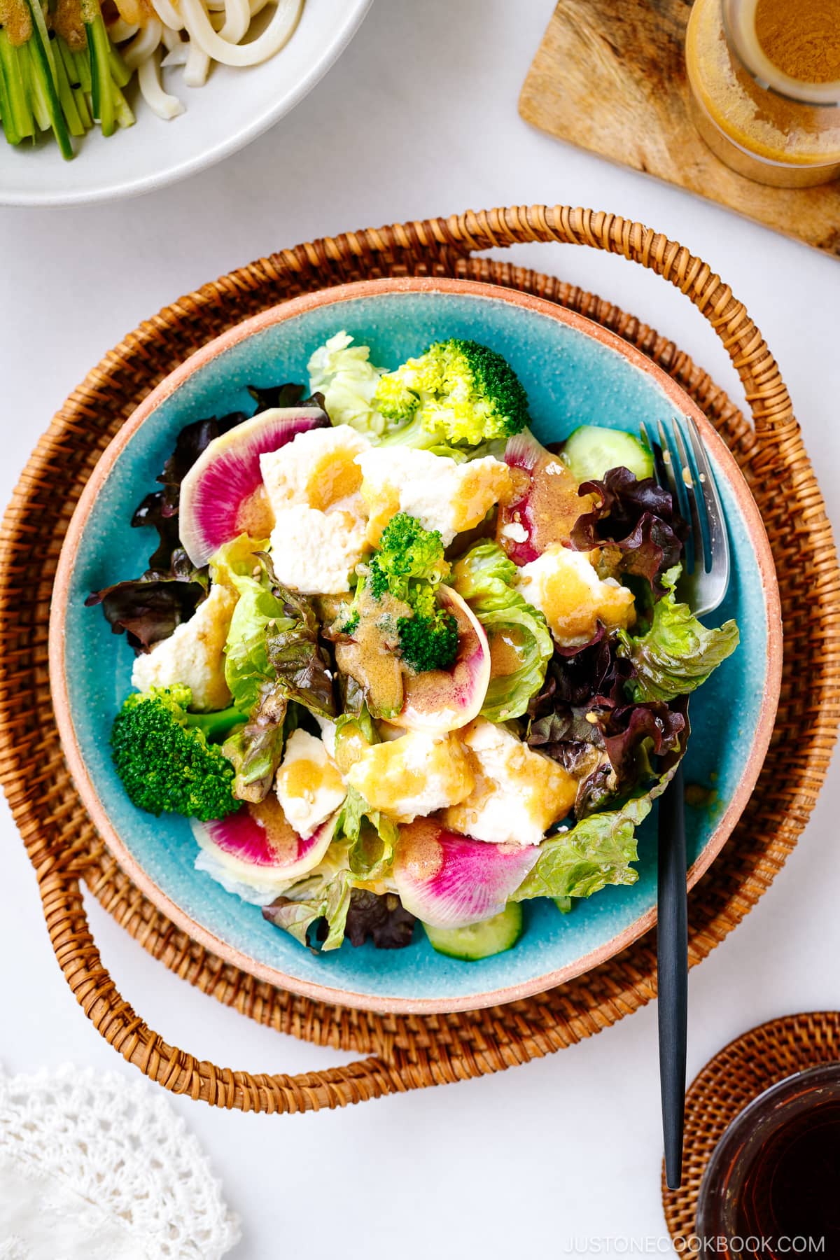 A blue ceramic plate containing green salad with tofu drizzled with homemade Miso Dressing.