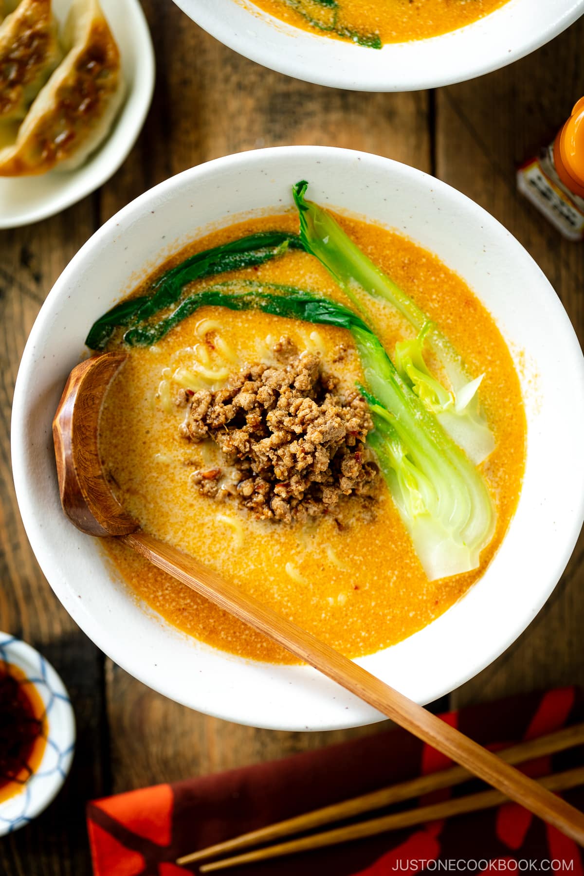 A white bowl containing Tan Tan Ramen (Tantanmen) which consists of ramen noodles and spicy creamy sesame soup, topped with savory ground pork mixture and blanched bok choy.