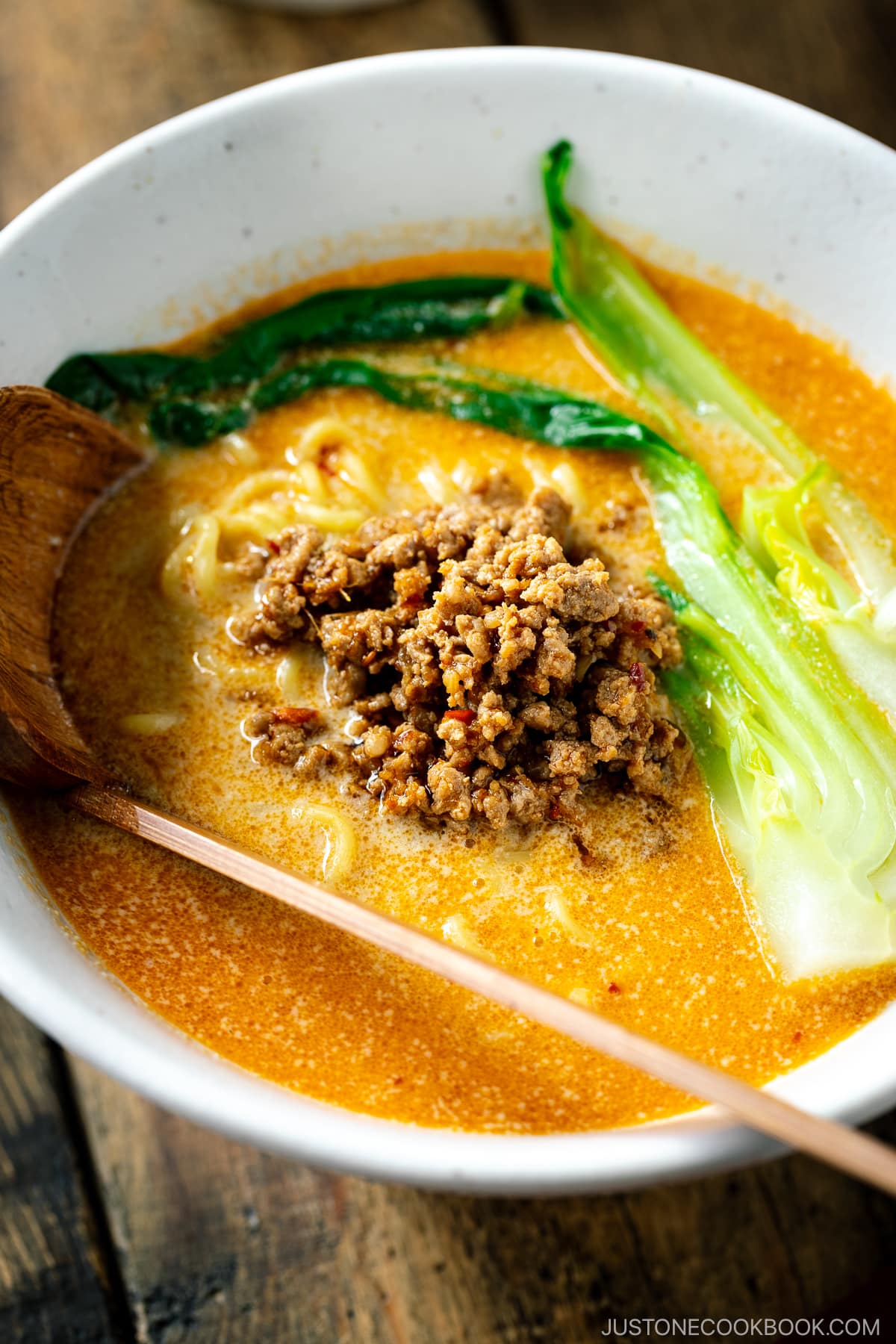 A white bowl containing Tan Tan Ramen (Tantanmen) which consists of ramen noodles and spicy creamy sesame soup, topped with savory ground pork mixture and blanched bok choy.