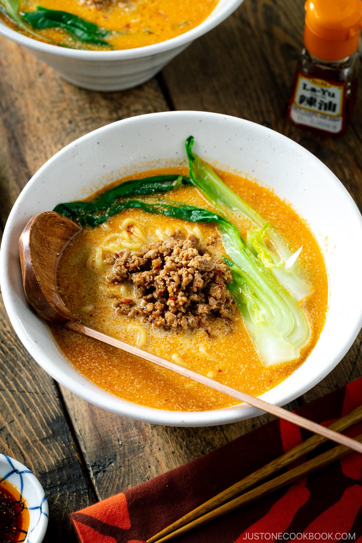 A white bowl containing Tan Tan Ramen (Tantanmen) which consists of ramen noodles and spicy creamy sesame soup, topped with savory ground pork mixture and blanched bok choy.