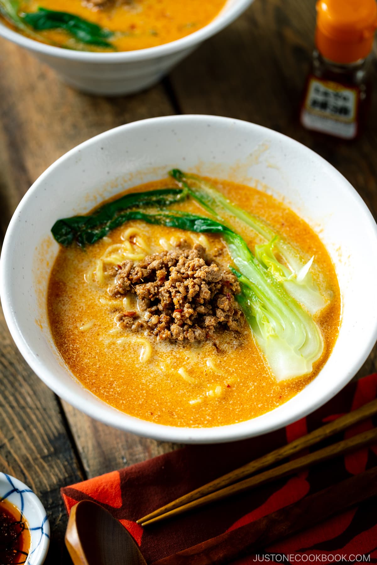 A white bowl containing Tan Tan Ramen (Tantanmen) which consists of ramen noodles and spicy creamy sesame soup, topped with savory ground pork mixture and blanched bok choy.