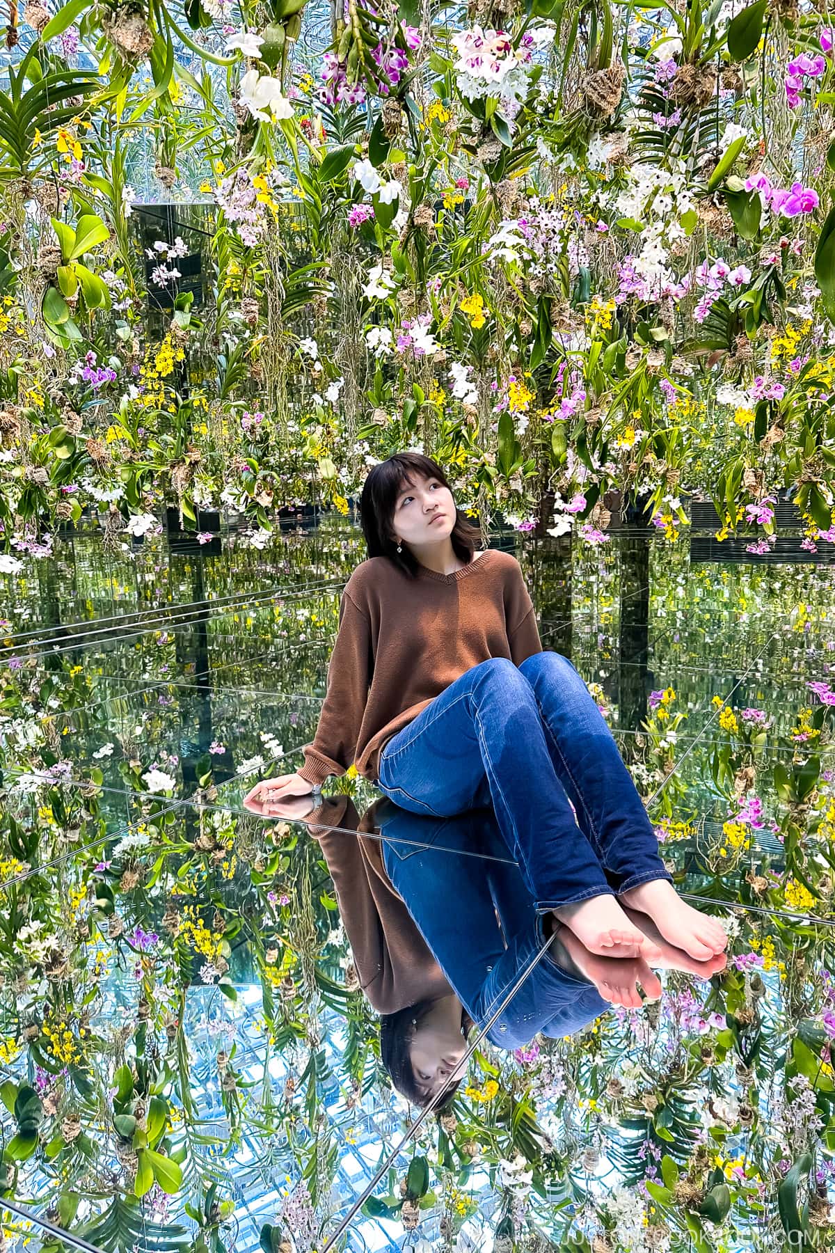 a girl sitting on mirror floor with dangling orchids