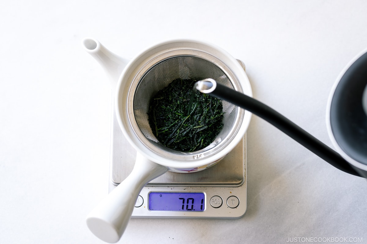 hot water being poured on tea leaves in a teapot