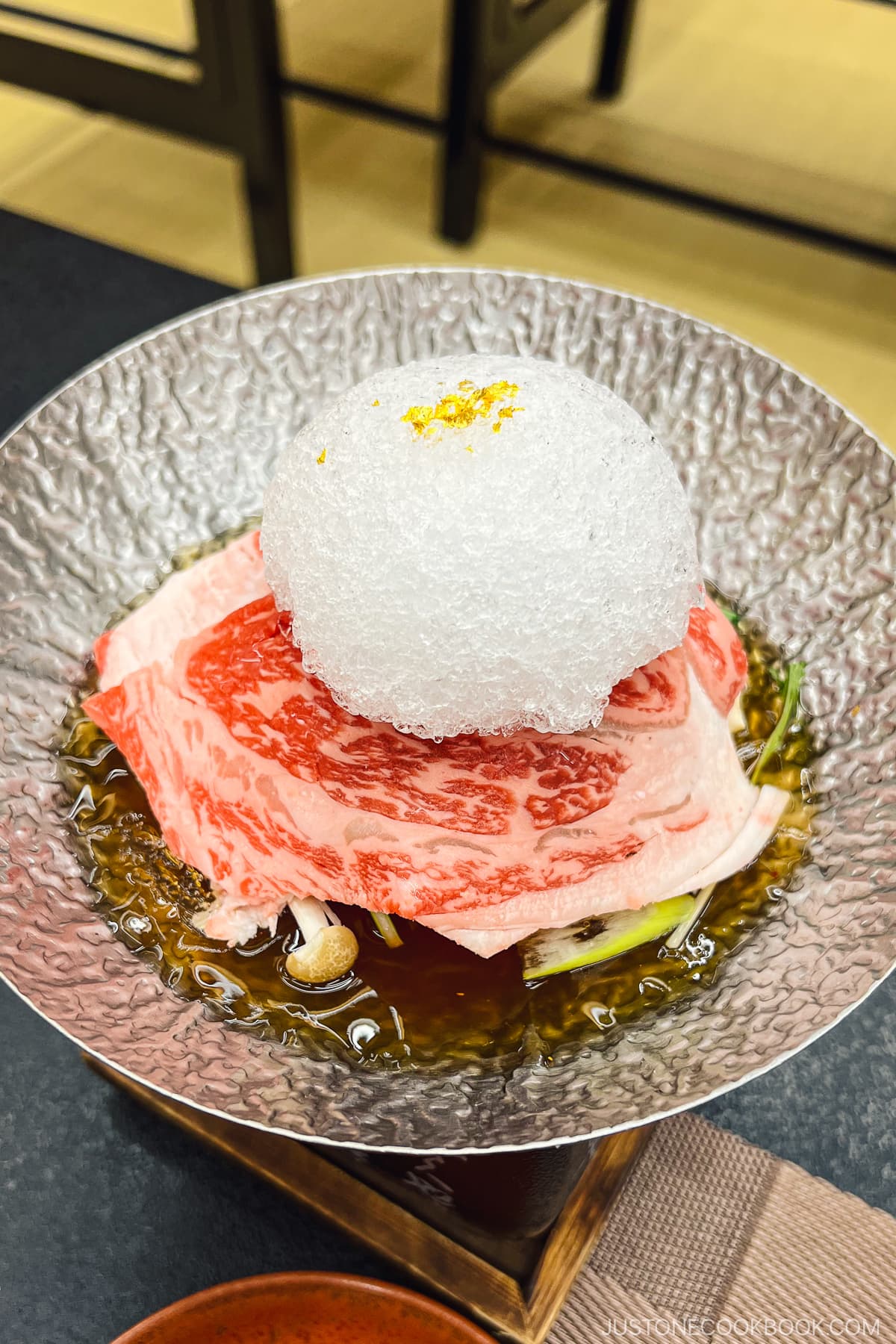 shaved ice on top of thinly sliced beef on top of a metal bowl